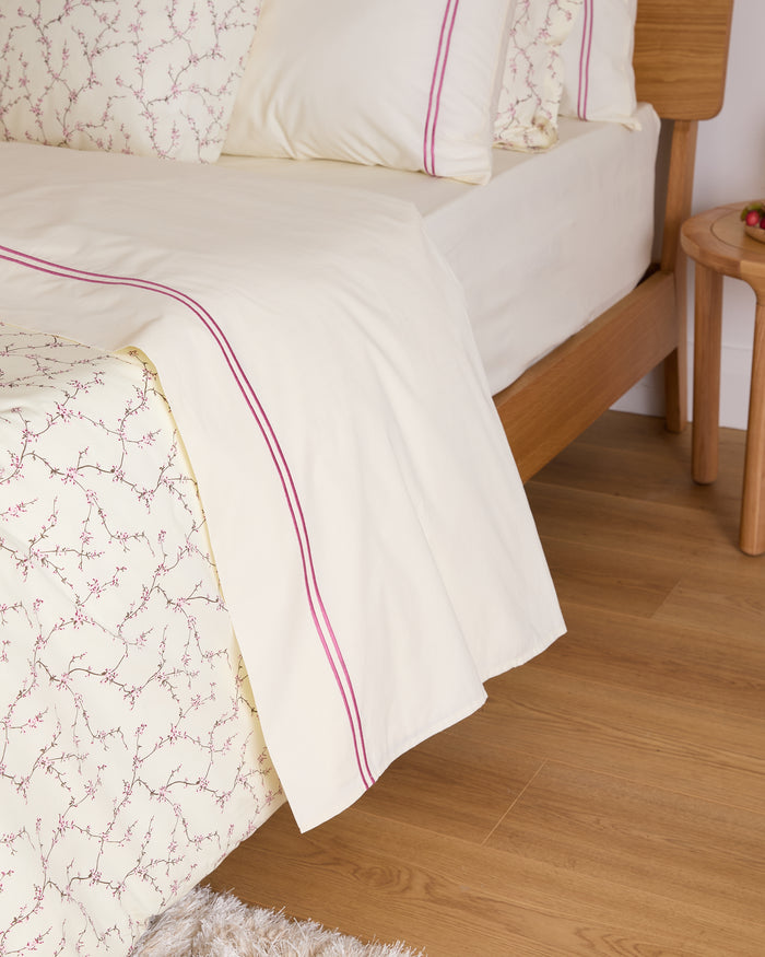 Bed with cream bedding and pink trim on a wooden floor.